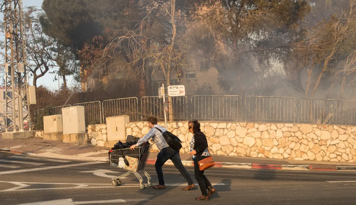 Warga mendorong troli saat menyelamatkan diri dari kebakaran hutan yang melanda kota utara Israel, Haifa, Kamis (24/11). Sekitar 80 ribu warga diminta meninggalkan rumah mereka karena kebakaran menyebar di kota terbesar ketiga Israel itu. (JACK GUEZ/AFP)