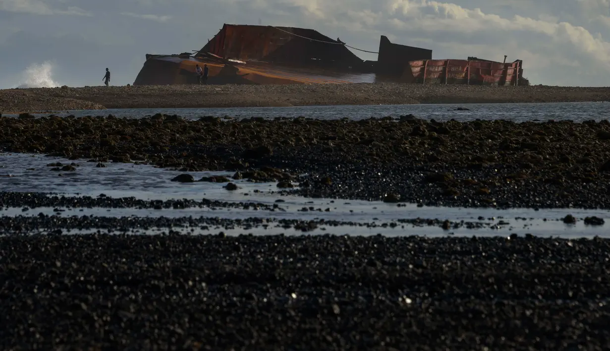 Pengunjung berjalan di pantai Lhoknga yang tercemar tumpahan batu bara dari kapal tongkang di Aceh, Rabu (1/8). Sekitar 7.000 ton batu bara tumpah dari kapal tongkang yang kandas dihantam gelombang sehingga merusak terumbu karang. (AFP/CHAIDEER MAHYUDDIN)