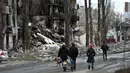 Orang-orang berjalan melewati bangunan yang hancur di kota Borodianka, barat laut Kiev pada 4 April 2022. Saat pasukan Rusia mundur, kota kecil Borodianka, 50 km barat laut Kiev, menjadi reruntuhan. (Sergei SUPINSKY / AFP)