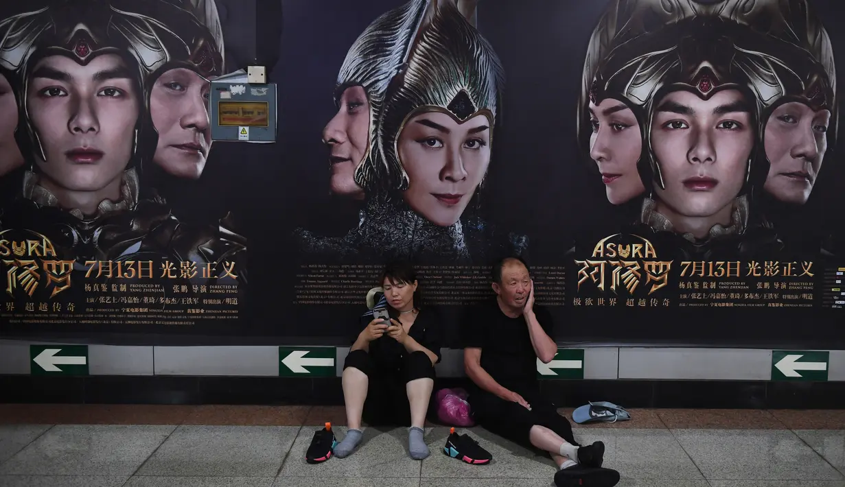 Seorang pria dan wanita beristirahat di depan poster film Asura di stasiun kereta bawah tanah di Beijing, Selasa (17/7). Film fantasi ini dilaporkan menelan biaya produksi sebesar 750 juta yuan (sekitar Rp1,6 triliun). (AFP/GREG BAKER)