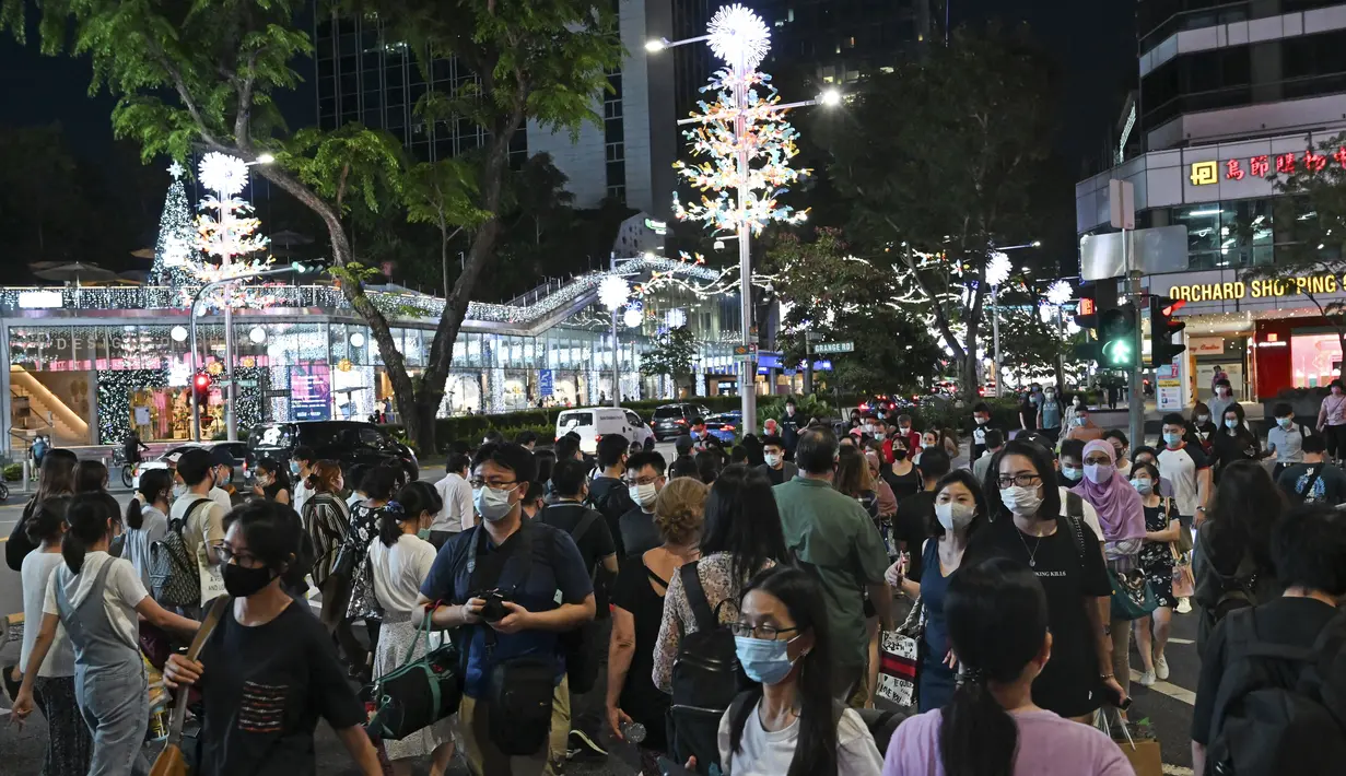 Pejalan kaki menyeberang jalan yang didekorasi dengan lampu Natal di distrik perbelanjaan Orchard road di Singapura, Selasa (8/12/2020). Mengusung tema Love This Christmas, acara tahun ini lebih sunyi karena aktivitas jalanan dibatasi di tengah pandemi Covid-19. (ROSLAN RAHMAN / AFP)