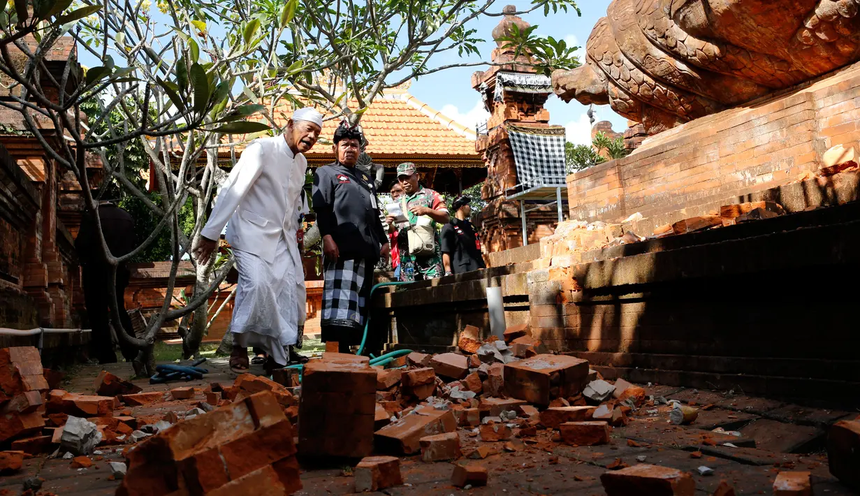 Pemuka agama dan prajurit TNI memantau kerusakan pada bagian candi yang runtuh akibat gempa di Pura Lokanatha, Denpasar, Bali, Selasa (16/7/2019). Gempa Magnitudo 5,8  yang mengguncang Bali dilaporkan terasa hingga ke Lombok dan wilayah Jawa Timur. (AP/Firdia Lisnawati)
