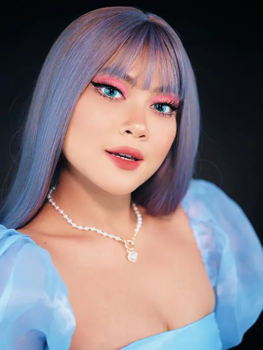 Bak Disney Princess, Hanum Mega totalitas memperlihatkan makeup looknya dengan wig biru keabu-abuan. Makeup bak Barbie dengan eyeshadow pink dan softlens biru yang kontras, Hanum Mega mengenakan wig dan outfit bak princess berwarna biru muda dan aksesori kalung. Foto: Instagram.