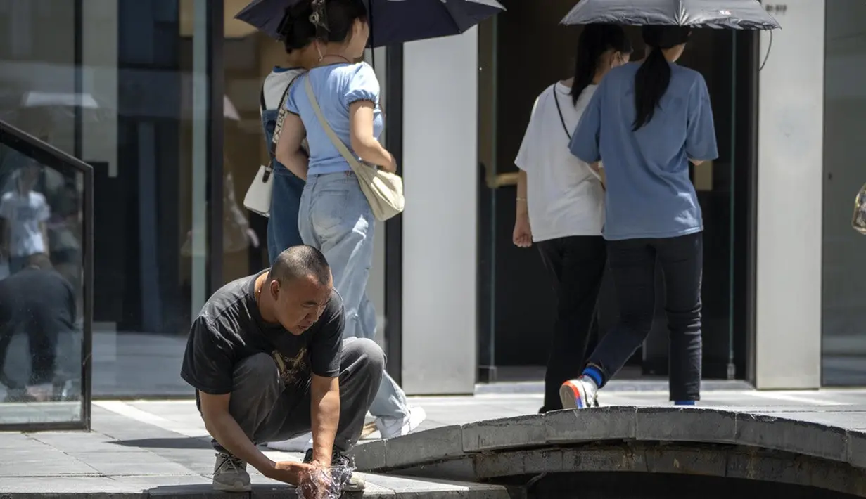<p>Sejumlah cara dilakukan oleh warga untuk mengurangi suhu panas yang melanda Beijing. Di antara mereka ada yang menggunakan payung saat berada di luar ruangan hingga ada juga yang menyegarkan diri dengan membasuh diri di kolam-kolam yang ditemui. (AP Photo/Mark Schiefelbein)</p>