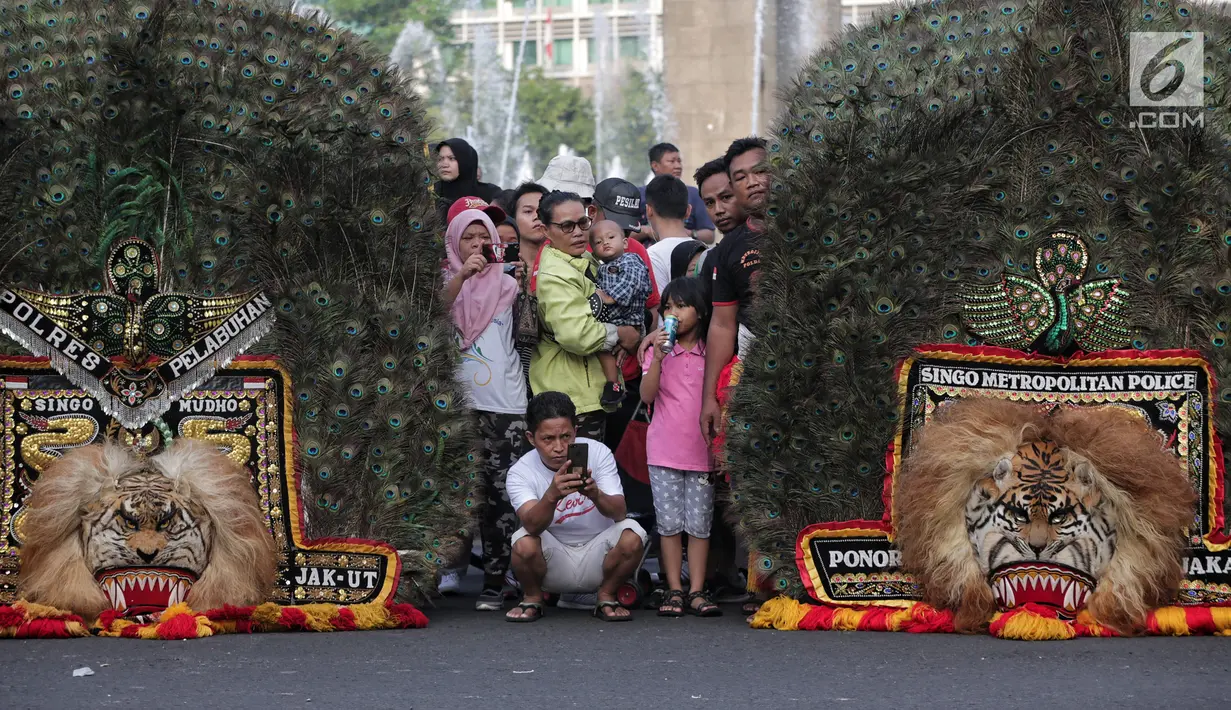 Pengunjung mengambil gambar pertunjukkan tari Reog Ponorogo di area car free day kawasan Bundaran Hotel Indonesia (HI), Jakarta, Minggu (28/4/2019). Kegiatan untuk memperingati Hari Kartini tersebut turut diramaikan oleh sejumlah polisi wanita (polwan). (Liputan6.com/Faizal Fanani)