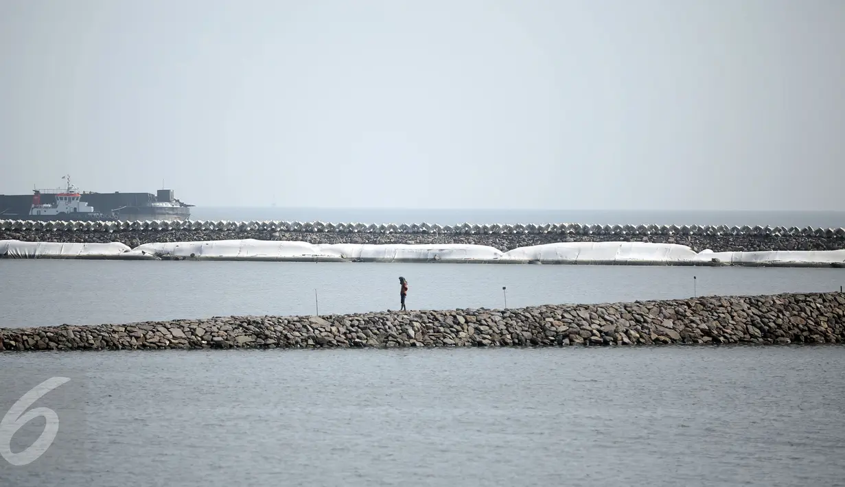 Seorang warga melintas diatas bebatuan tanggul pemecah ombak di Pantai Ancol, Jakarta, Minggu (24/4/2016). Tanggul ini diperuntukan mencegah banjir rob yang sudah sering menimpa daerah Jakarta Utara dan sekitarnya.(Liputan6.com/Faizal Fanani)