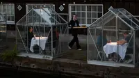 Staf menggunakan papan panjang untuk menyajikan makanan kepada pelanggan dalam kabin kaca "quarantine greenhouses" selama uji coba, ketika Belanda berjuang melawan penyebaran COVID-19, di restoran Mediamatic, Amsterdam pada 5 Mei 2020. (AP/Peter Dejong)