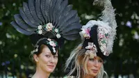 Dua wanita memakai hiasan kepala berpose saat tiba untuk menyaksikan balap kuda Royal Ascot horse di Ascot, London, (20/6). Mereka tampil gaya saat menyaksikan kompetisi balap kuda ini. (AFP Photo/Daniel Leal-Olivas)