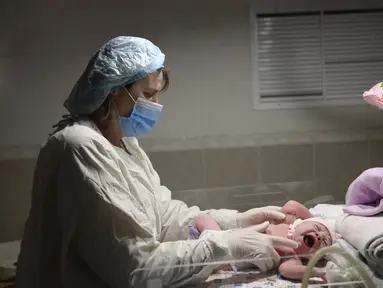Seorang perawat memeriksa bayi Aleina Snizhana yang melahirkan di bangsal bersalin saat peringatan sirene untuk serangan udara di Mykolaiv, Ukraina pada 14 Maret 2022. Hampir setengah dari 49 perempuan harus melahirkan di ruang bawah tanah sejak 24 Februari lalu. (BULENT KILIC/AFP)