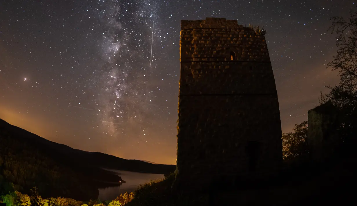 Sebuah meteor melintasi langit malam di sebelah Bima Sakti selama hujan meteor tahunan Perseid di danau Pierre-Percee, Perancis timur, Minggu (12/8). Puncak hujan meteor terjadi pada 11-12 Agustus dan 12-13 Agustus. (Patrick HERTZOG / AFP)