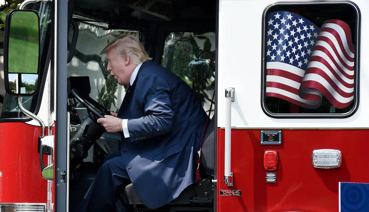 Presiden AS, Donald Trump duduk sambil memeriksa sebuah truk pemadam kebakaran saat bersama Wapres Mike Pence menghadiri acara pameran produk bertajuk "Made in America" di Gedung Putih, Washington, Senin (17/7). (Olivier Douliery/AFP)