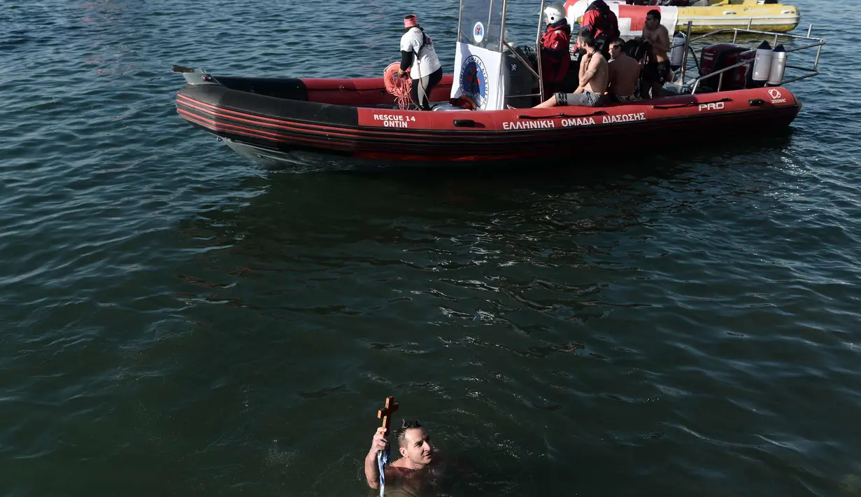 Seorang perenang memegang sebuah salib kayu yang dilemparkan ke laut saat restu upacara air menandai hari Epiphany Orthodox, di pelabuhan Thessaloniki, Yunani utara, (6/1). (AFP Photo/Sakis Mitrolidis)