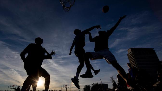 Orang-orang bermain bola basket saat matahari terbenam di sebuah lapangan di pusat Vilnius, Lithuania, Rabu, (15/7 2020). (AP Photo/Mindaugas Kulbis)  