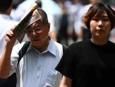 Seorang pria melindungi dirinya dari sinar matahari dengan sebuah koran saat gelombang panas di Tokyo, Jepang (1/7/2019). Cuaca panas ekstrem yang melanda Jepang telah menewaskan puluhan orang tewas dan menyebabkan ribuan orang masuk rumah sakit dengan gejala dehidrasi. (AFP Photo/Charly Triballeau)