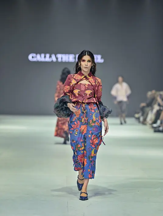 Lalu, ada Sabrina Chairunnisa yang turut unjuk gigi di runway. Ia mengenakan atasan merah dengan aksen scrunchie di lengannya. Atasan tersebut ia padukan dengan rok berpotongan pensil motif floral senada. [Foto: Instagram/callathelabel & Getty Images/JFW Official]