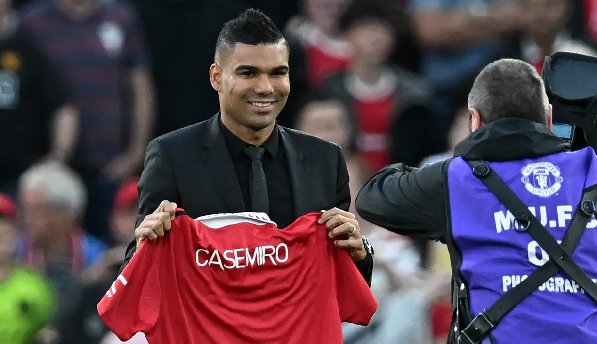 Casemiro yang berpakaian serba hitam, mulai dari jas sampai kemeja yang dikenakannya, berjalan menuju tengah lapangan. Di sana, ia memamerkan jersey barunya yang masih belum ada nomor punggungnya itu. (AFP/Paul Ellis)