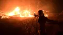 Seorang pria menggunakan selang air saat kebakaran hutan di daerah Adames, utara Athena, Yunani, Selasa (3/8/2021). Gelombang panas membuat suhu mencapai 42 derajat Celcius (107,6 Fahrenheit) di beberapa bagian Ibu Kota Yunani. (AP Photo/Michael Varaklas)
