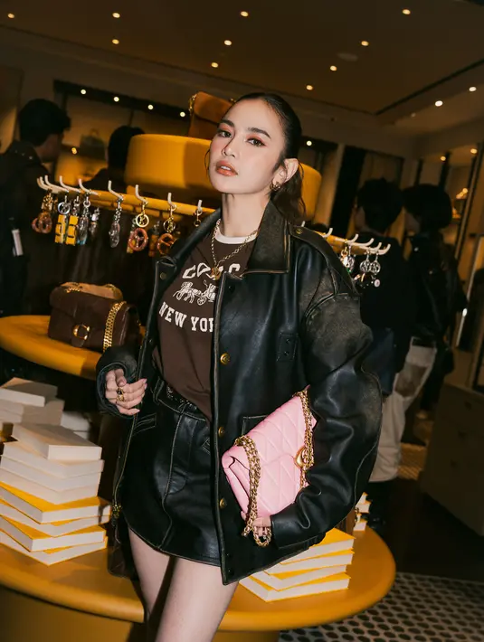 Sentuhan kaus grafis memberi kesan kasual yang kontras, sementara tas Tabby berwarna pink dengan aksen chain strap menjadi highlight yang langsung menarik perhatian. Look ini terasa effortless, tapi tetap polished, mencerminkan perempuan modern yang percaya diri dengan gayanya sendiri.  [Dok/KANMO GROUP].