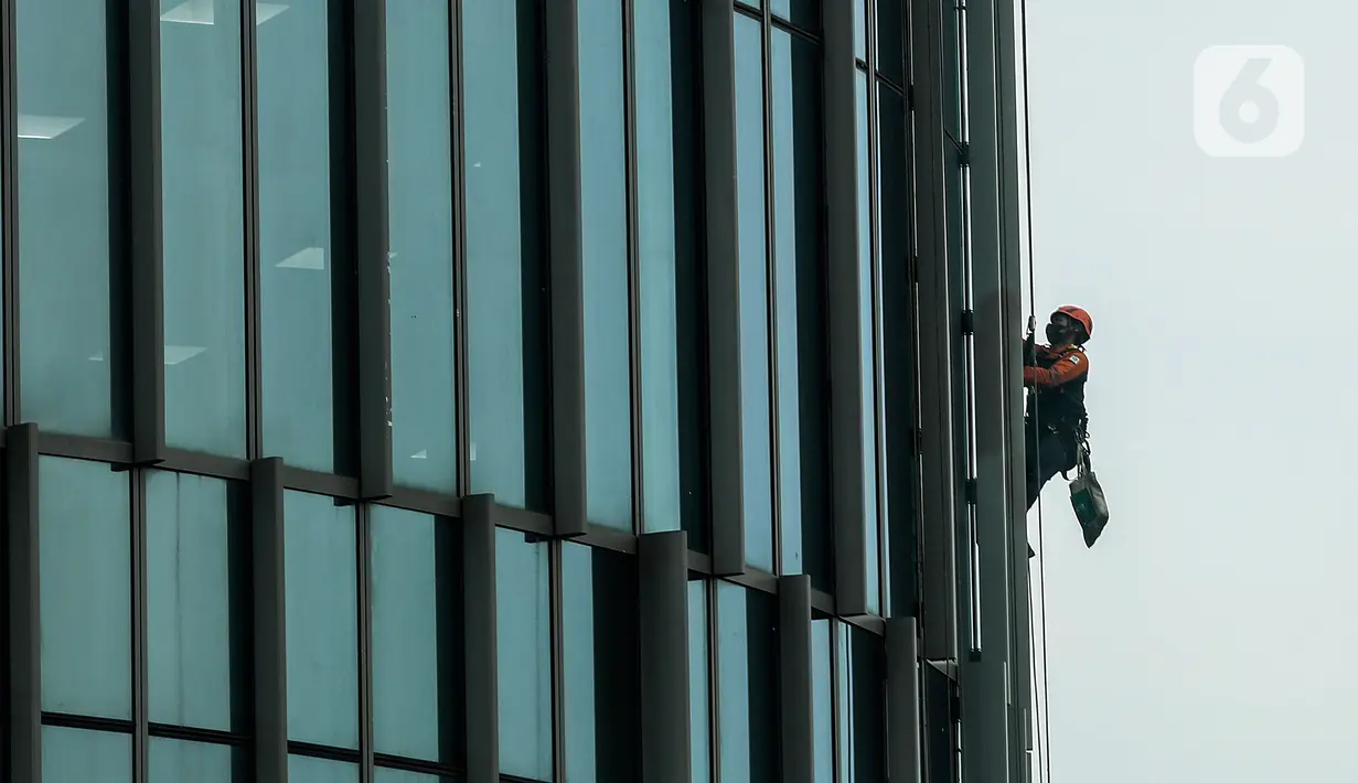 Pekerja saat membersihkan kaca gedung bertingkat di kawasan Kuningan, Jakarta, Minggu (19/12/2021). Pekerja ini harus bergelantungan dengan seutas tali untuk membersihkan dinding-dinding gedung bertingkat yang tingginya kurang lebih mencapai 150 meter. (Liputan6.com/Johan Tallo)
