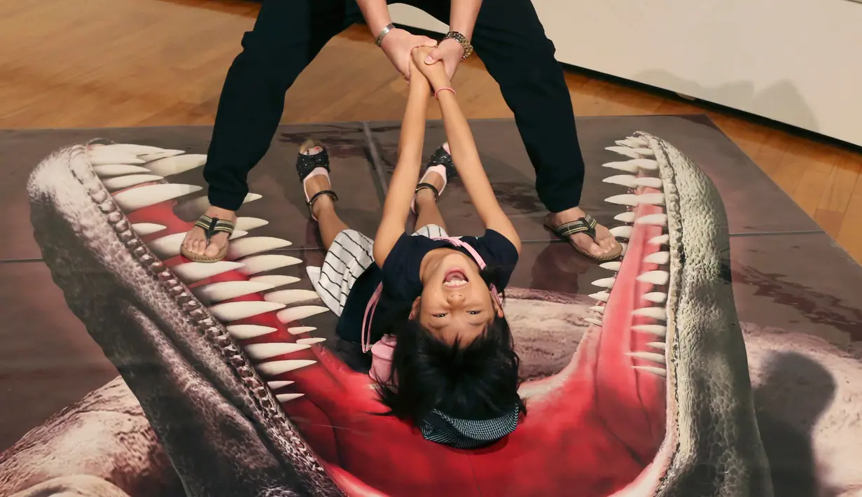 Seorang anak berpose dengan gambar 3D dinosaur pada pameran seni trik 3D karya seniman Jepang Masashi Hattori di Kawasaki, dekat Tokyo, Sabtu, (5/8). (AP Photo / Koji Sasahara)