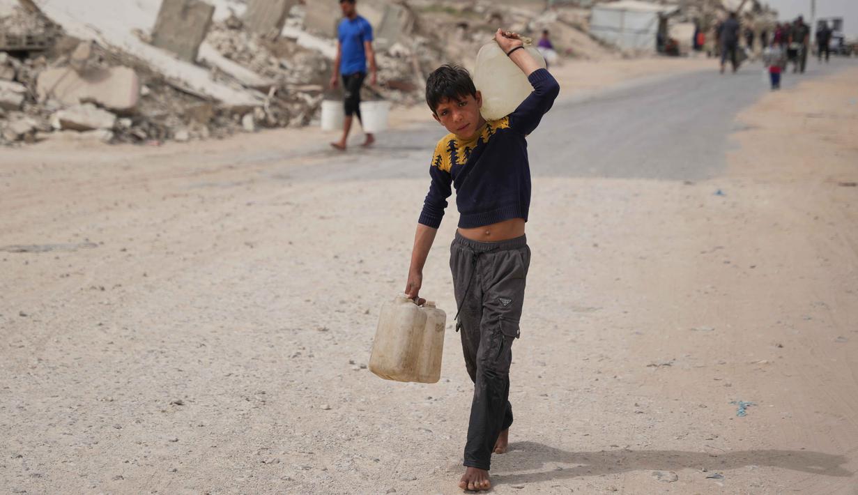 Saat ini, di antara infrastruktur yang runtuh dan sumber daya yang menipis, warga Gaza bergantung pada bantuan air terbatas, yang distribusinya sering terhambat oleh situasi keamanan. Tampak dalam foto, seorang pemuda Palestina membawa wadah air di Kota Gaza, Selasa 12 Mei 2026. (AP Photo/Abdel Kareem Hana)