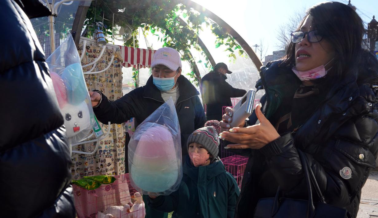 Pelanggan membeli benang gula di toko popup, Beijing, China, 27 Desember 2022. Perusahaan menyambut baik keputusan China untuk mengakhiri karantina bagi pelancong dari luar negeri sebagai langkah penting untuk menghidupkan kembali aktivitas bisnis yang merosot, sementara Jepang mengumumkan pembatasan pengunjung saat infeksi melonjak. (AP Photo/Ng Han Guan)