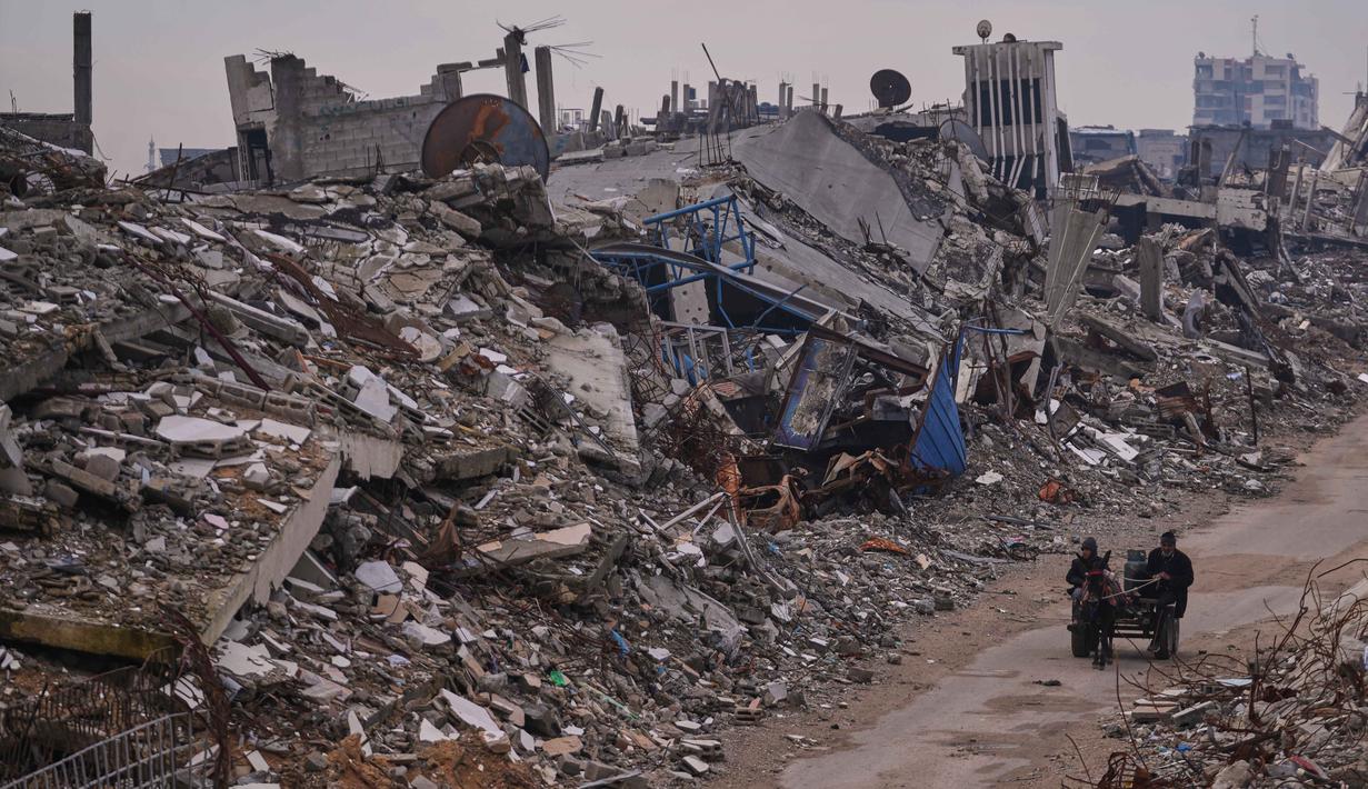 Data Shelter Cluster Gaza yang dikutip UNRWA mencatat, hujan deras dan angin kencang akibat tekanan cuaca rendah pada 10–17 Desember 2025 menyebabkan 17 bangunan runtuh serta merusak lebih dari 42.000 tenda dan hunian darurat, baik sebagian maupun total. Tampak dalam foto, warga Palestina berjalan di sepanjang jalan yang dikelilingi bangunan-bangunan yang hancur akibat serangan udara dan darat Israel di lingkungan Sheikh Radwan, Kota Gaza, Selasa, 30 Desember 2025. (AP Photo/Abdel Kareem Hana)