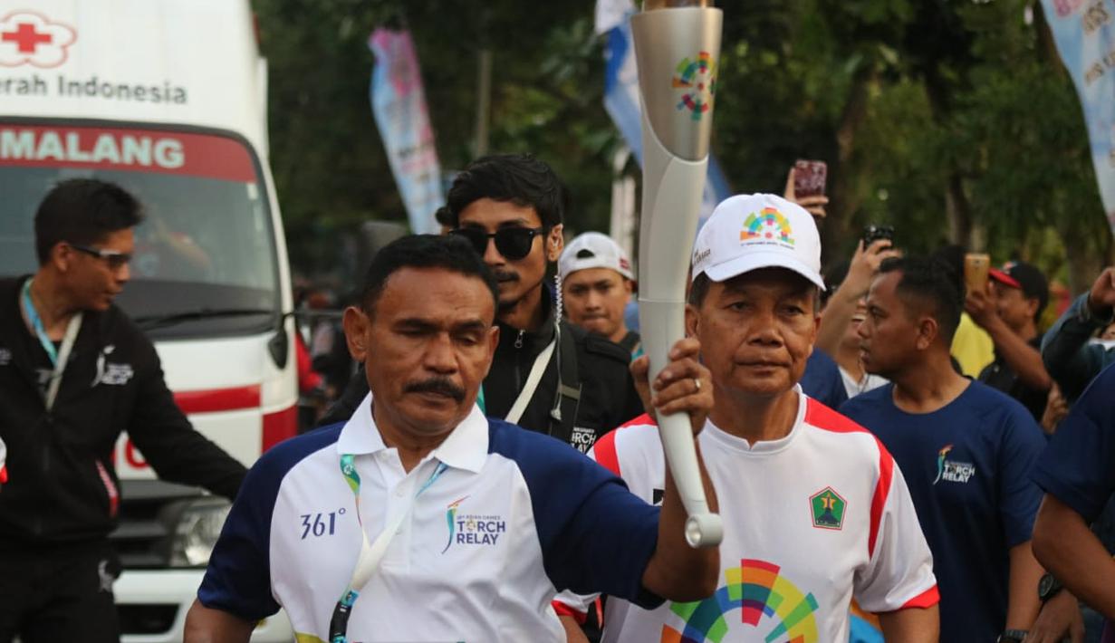 Petinju legendaris Indonesia, Nico Thomas, membawa obor Asian Games XVIII saat melintasi di Kota Malang, Jawa Timur, Jumat (20/7/2018). Sebanyak 10 kota di Indonesia akan dilalui oleh obor Asian Games. (Bola.com/Aditya Wany)
