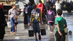 Seorang pemuda Palestina membawa ember-ember air yang diisi di titik pengambilan air di kamp pengungsi Nuseirat, yang terletak di Jalur Gaza tengah, pada 2 November 2025. Selain itu, sekitar 650.000 anak perlu segera kembali bersekolah. Hal tersebut dinyatakan Tess Ingram pada Minggu 2 November 2025. (EYAD BABA/AFP)