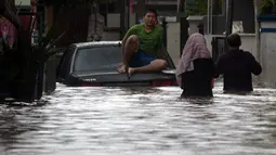 Warga duduk di atas mobil saat banjir merendam jalan dan rumah di RT 003/05, Pejaten, Jakarta, Sabtu ( 20/2/2021). Curah hujan yang tinggi sejak malam hingga dini hari mengakibatkan sejumlah kawasan terendam banjir. (merdeka.com/Imam Buhori)