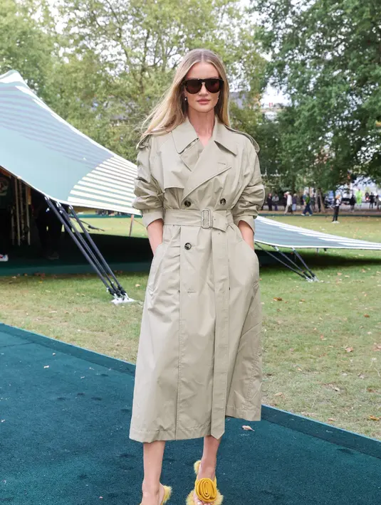 Aktris Rosie Huntington-Whiteley tampil anggun dengan trench coat warna beige yang dipadukan dengan sandal bunga warna kuning yang mencolok. [Dok/Burberry]