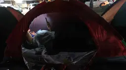 Mereka dengan cemas menanti pembebasan tahanan politik yang telah dijanjikan. Tampak dalam foto, seorang wanita menggunakan telepon seluler di atas tenda yang didirikan oleh kerabat tahanan politik di luar penjara El Rodeo I di Guatire, Negara Bagian Miranda, sekitar 30 kilometer sebelah timur Caracas, Venezuela, pada 12 Januari 2026. (Pedro MATTEY/AFP)