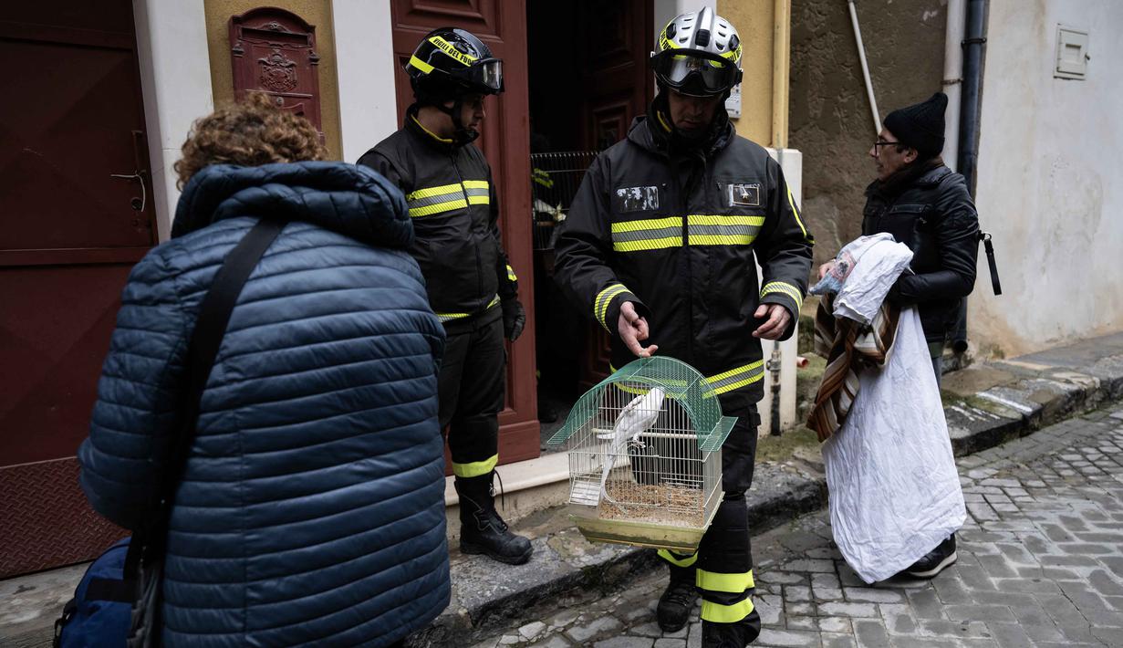 Para ahli mengatakan jurang tersebut dapat melebar lebih jauh dan meruntuhkan rumah-rumah dengan hujan yang diperkirakan akan turun dalam beberapa hari mendatang. Tampak dalam foto, petugas pemadam kebakaran membantu para pengungsi menyelamatkan burung beo dari sebuah rumah dan mengumpulkan barang-barang mereka di zona merah Niscemi, Sisilia, Kamis 29 Januari 2026. (MARCO BERTORELLO/AFP)