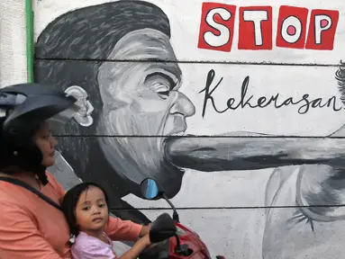 Pengendara sepeda motor melintas di sisi tembok yang terdapat lukisan mural di kawasan Kramat Jati, Jakarta, Rabu (4/4). Kawasan ini mendapat julukan Kampung Mural. (Liputan6.com/Herman Zakharia)