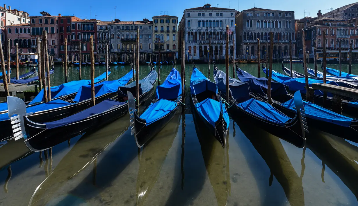 Perairan yang lebih jernih terlihat saat sejumlah gondola terparkir di Grand Canal Venesia pada 18 Maret 2020. Sejak Italia memberlakukan lockdown akibat pandemi virus corona, air di Kanal Venesia yang biasanya keruh dan gelap berubah menjadi jernih. (ANDREA PATTARO / AFP)