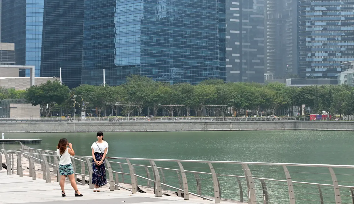 Seorang wanita saat difoto dengan rekannya di sepanjang kawasan pejalan kaki di Marina Bay di Singapura (13/9/2019). Kebakaran hutan yang terjadi di Indonesia membuat kekhawatiran tentang dampak meningkatnya wabah api di seluruh dunia pada pemanasan global. (AFP Photo/Roslan Rahman)