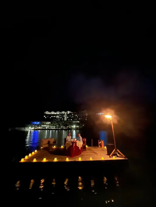Dinnar romantis di tengah laut dengan dikelilingi lampu dipinggir. Dua dekade lebih menikah, keduanya masih bisa menjaga kemesraannya bak pengantin baru. [Instagram/bu_deedee]