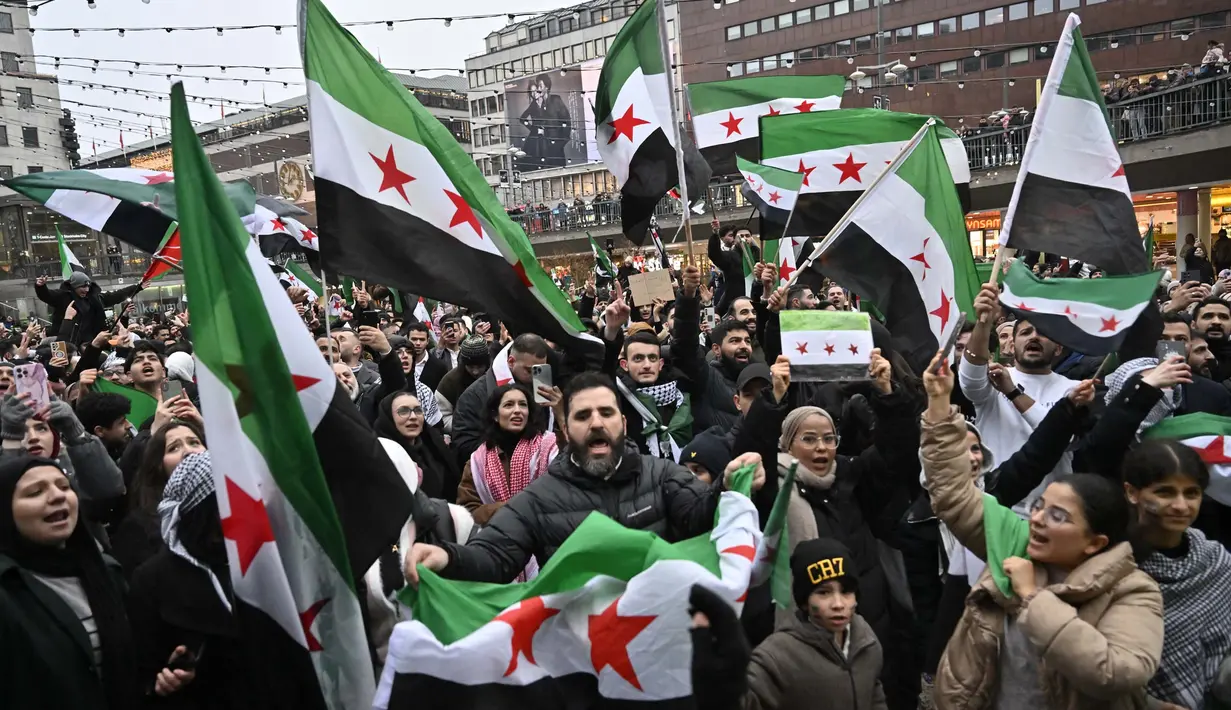 Kekuasaan keluarga Assad di Suriah runtuh dengan sangat cepat setelah kelompok pemberontak keluar dari wilayah yang dikuasainya. Tampak dalam foto, anggota komunitas Suriah memegang bendera oposisi Suriah saat mereka berkumpul pada tanggal 8 Desember 2024 di Sergel's Square di Stockholm, Swedia. (Jonas EKSTROMER/TT News Agency/AFP)