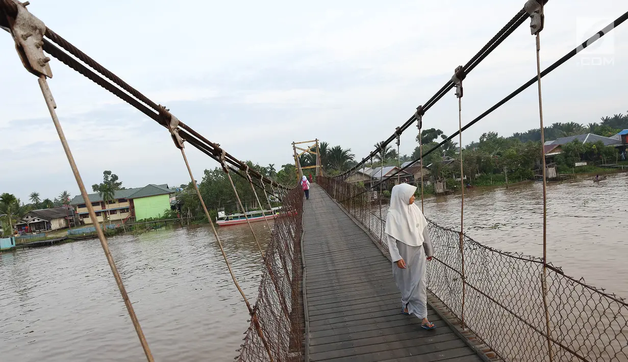 Warga melintasi jembatan penyeberangan di Sungai Martapura, Banjarmasin, Kalimantan Selatan, Selasa (27/3). Walaupun menjadi jembatan satu-satunya untuk akses menyeberang warga sekitar, kondisi jembatan terlihat seadanya. (Liputan6.com/Immanuel Antonius)