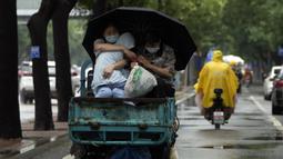 Seorang wanita yang mengenakan masker menggendong seorang anak saat dia mendapat tumpangan saat hujan di Beijing, China, 12 Juli 2022. Beijing telah membatalkan rencana untuk mengizinkan hanya orang yang divaksinasi yang memasuki ruang publik. (AP Photo/Ng Han Guan)