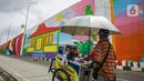Seorang pedagang melintasi mural yang dibuat di Flyover Gaplek, Tangerang Selatan, Rabu (10/3/2021). Konsep muralnya adalah "Tangsel Membangun". (Liputan6.com/Faizal Fanani)