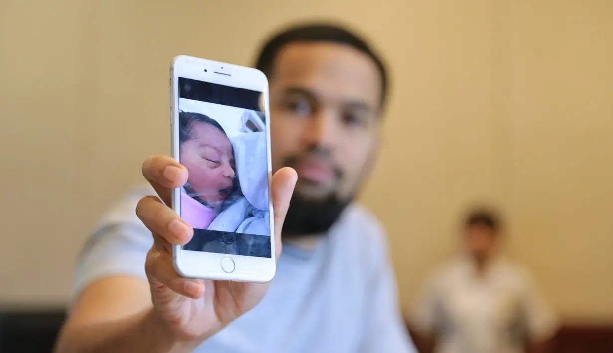 Wisnu menunjukkan foto melalui handphone yang dipegangnya. Foto anak ketiga perempuan yang diberi nama Cut Shafiyyah Mecca Alfatih. (Adrian Putra/Bintang.com)