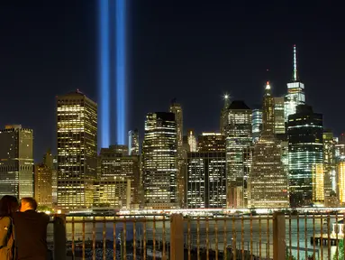 Sepasang kekasih menikmati ‘Tribute in Light’ dari sisi Brooklyn Promenade untuk mengenang tragedi serangan WTC di New York, Minggu (10/9). Kota New York memperingati 16 tahun tragedi serangan bom pada 11 September 2001 silam. (AP Photo/Mark Lennihan)