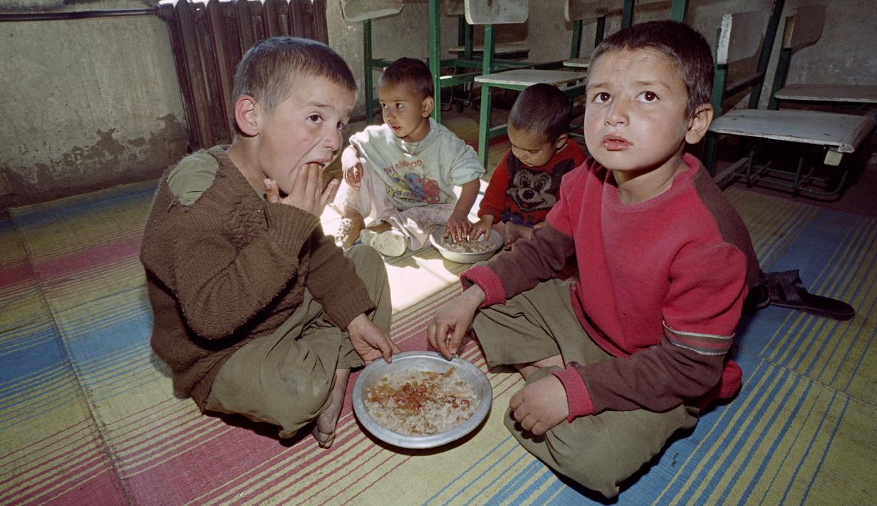 Anak-anak makan nasi di sebuah kamar di panti asuhan terakhir yang tersisa di Kabul, Afghanistan, 26 Oktober 1996. Ratusan anak menghadapi pertempuran untuk bertahan hidup setelah pemimpin baru Taliban di Kabul melarang perempuan bekerja dan memotong dana untuk panti asuhan. (SAEED KHAN/AFP)