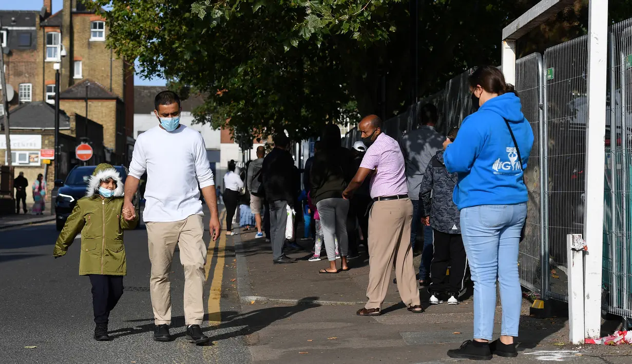 Orang-orang, beberapa memakai masker, mengantre untuk memasuki pusat pengujian virus corona di Edmonton, utara London, Kamis (17/9/2020). PM Inggris Boris Johnson mengatakan dirinya bisa menutup pub-pub lebih awal sebagai pencegahan kenaikan kasus Covid-19 untuk kedua kalinya. (JUSTIN TALLIS/AFP)
