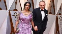 Salma Hayek dan suami, Francois-Henri Pinault  menghadiri karpet merah Piala Oscar 2018 di Los Angeles, Minggu (4/3). Tambahan aksesori seperti clutch silver dan anting chandeliernya pun membuat tampilan Salma cukup stunning. (Jordan Strauss/Invision/AP)