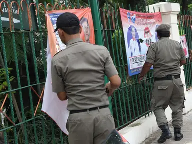 Petugas Satpol PP bersama Panwaslu kecamatan Ciracas menurunkan APK yang terpasang di pagar pembatas antara jalan dengan taman di pinggir kali di sekitar Jalan Raya Bogor, Jakarta, Rabu (23/1). (Liputan6.com/Helmi Fithriansyah)
