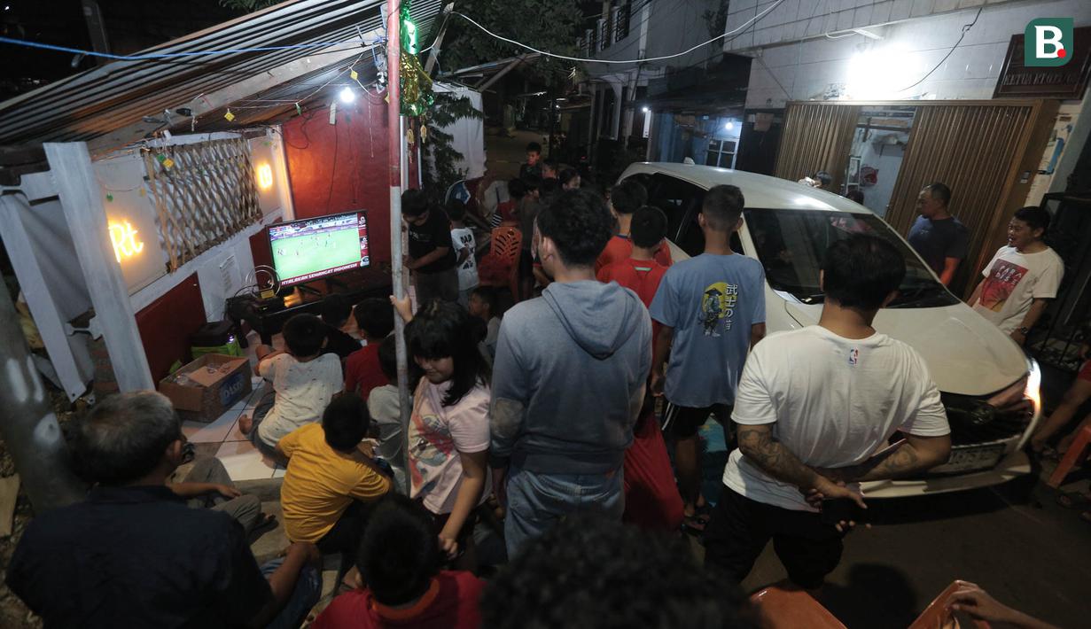 Sejumlah warga terpaksa bangkit dari duduknya saat mobil melintas di lokasi nobar pertandingan Timnas Indonesia melawan Bahrain dalam pertandingan Grup C putaran ketiga Kualifikasi Piala Dunia 2026 zona Asia di kawasan Menteng Jaya, Jakarta, Selasa (25/5/2025). (Bola.com/M Iqbal Ichsan)