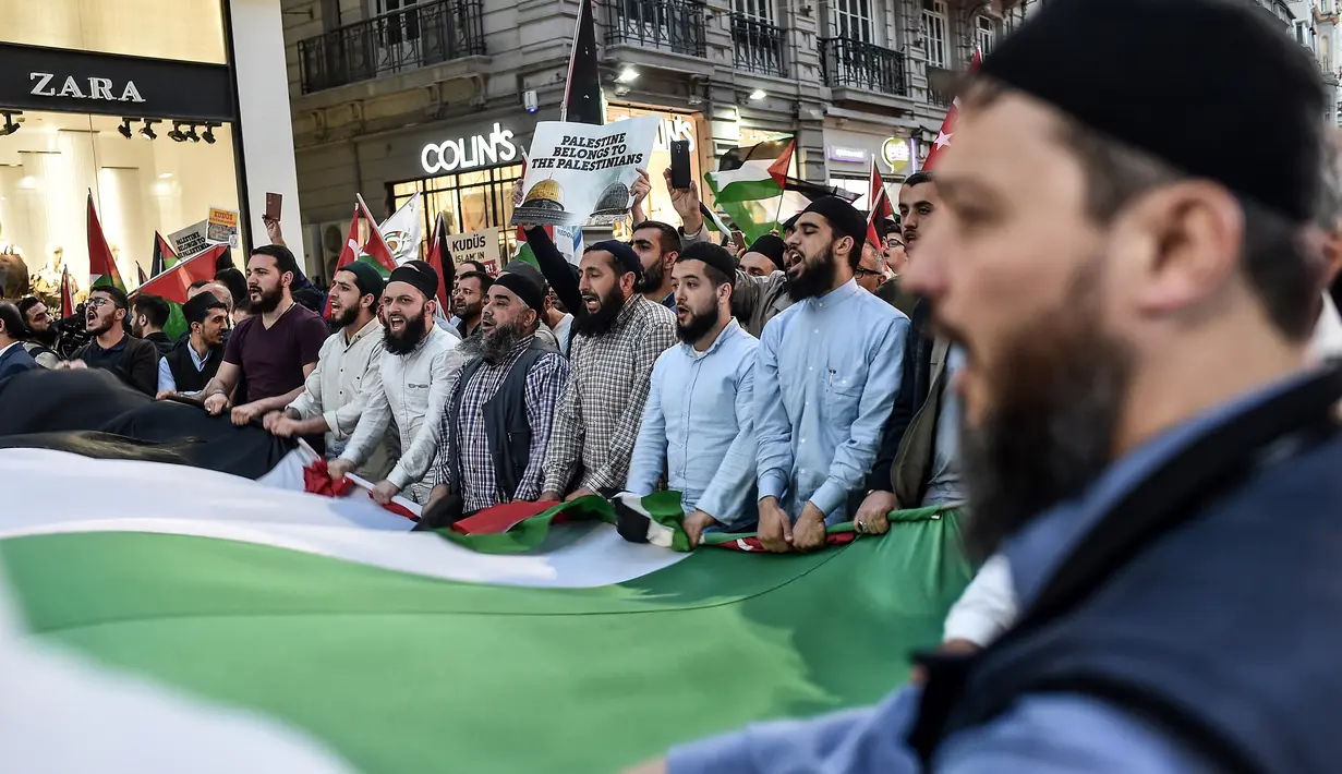 Para pengunjuk rasa membentangkan bendera Palestina saat menggelar aksi menolak perpindahan kedutaan AS dari Tel Aviv ke Yerusalem di Istikilal di Istanbul, Turki (14/5). (AFP/Ozan Kose)
