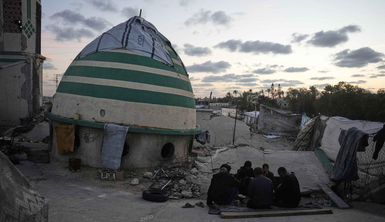 Meski berada di tengah puing-puing dan duka, momen berbuka puasa tetap dirayakan sebagai simbol kekuatan iman dan kebersamaan keluarga di Gaza. Tampak dalam foto, keluarga Suleiman berbuka puasa di bulan suci Ramadan di samping reruntuhan masjid, tempat mereka saat ini berlindung di Deir al-Balah, Jalur Gaza, Jumat 6 Maret 2026. (AP Photo/Abdel Kareem Hana)